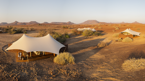 Designed for desert wanderers, Wilderness Desert Rhino Camp offers an original, exclusive wilderness experience and the opportunity to see free-ranging desert-adapted black rhino. The desert plains are starkly scenic, and home to other unique species, from Hartmann’s zebra and giraffe, to the bizarre welwitschia plant.

Styled with the desert in mind, the palette, textures and wildlife of Damaraland’s extraordinary vistas are brought into the elegant suite interiors.

With natural stone found on site reinforcing the camp’s connection to nature, Desert Rhino Camp evokes a real sense of place in this stark desert landscape.

Six suites with deep overhanging stretch fabric roof structures, interior tones of terracotta, sage, fern greens and cream, complemented by classic details of timber and leather, create a sheltered sanctuary within this breath-taking desert landscape.

Run in conjunction with Save the Rhino Trust Namibia, Wilderness Desert Rhino Camp offers rhino tracking by vehicle and on foot with experts from this conservation NGO.

Insider's Tip: Explore this extraordinary landscape in search of desert-adapted wildlife and gain amazing insight into the ecology and conservation of this area. A picnic lunch is the perfect complement to your day’s outing!